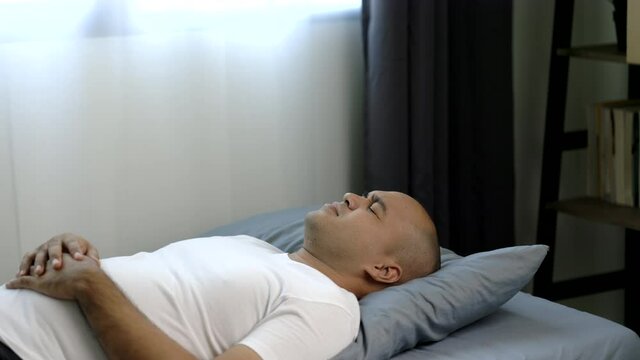 Asian bald man around the age of 30 in a white T-shirt can't sleep well. He had back pain and neck pain that he couldn't sleep.
