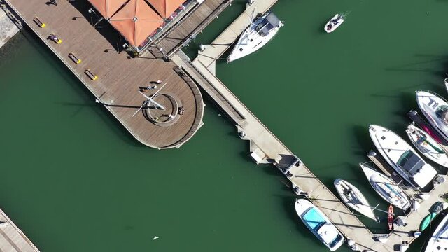 Top down view of dock and harbor with boats docked on a sunny day at Jack London Square.  Drone video Shot at 45 degree angle and slowly rising to expose more of the docks.