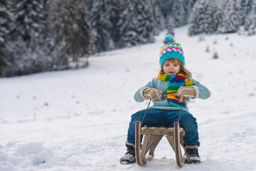 Fototapeta na wymiar Happy kid ride on sled. Active winter outdoors. Happy Christmas. Winter children. Little boy having fun in the snow. Winter greeting card, banner, poster.