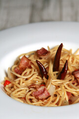 Spaghetti Aglio Olio with bacon, dried peppers and garlic. Lighting bokeh on the table.
