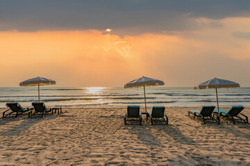 Sun umbrellas and chairs on tropical beach with sunset