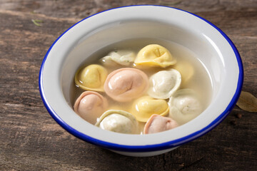 Traditional Russian dumplings made from multi-colored dough in broth. Dumplings on a wooden board in an enamel plate. Cooking concept.