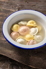 Traditional Russian dumplings made from multi-colored dough in broth. Dumplings on a wooden board in an enamel plate. Cooking concept.
