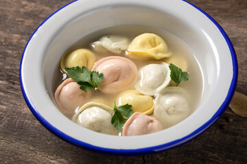 Traditional Russian dumplings made from multi-colored dough in broth. Dumplings on a wooden board in an enamel plate. Cooking concept.