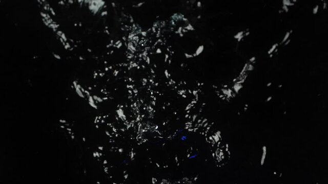 An action camera splashes in slow motion in black water.