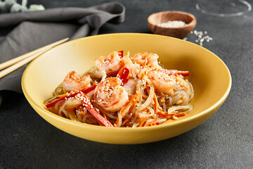 Asian Stir Fried Shrimp and Rice Noodles. Sesame Rice Noodles with Shrimp in yellow plate with wooden chopstick on dark slate table. Asian, authentic food concept