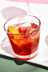 Negroni cocktail over pink background. Drink in rox glass in daylight with palm leaf hard shadow. Summer, tropical, fresh drink concept