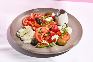 Tomato, olives and mozzarella salad . Restaurant appetizer plate on white table with pink wall. Day sunlight with hard shadow of fern palm leaves. Summer or spring restaurant food concept