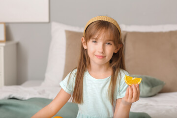 Cute little girl with piece of orange in bedroom