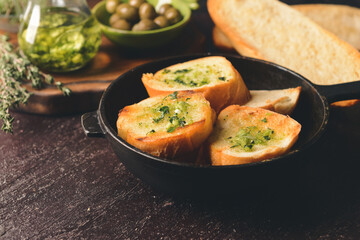 Frying pan of toasted bread with garlic on dark background
