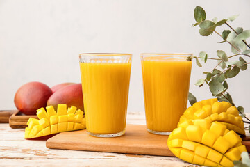 Glasses of tasty mango smoothie on light wooden background