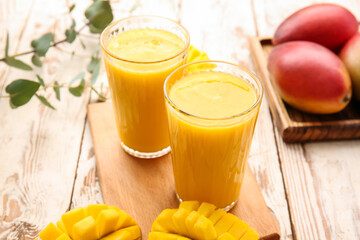 Glasses of tasty mango smoothie on light wooden background