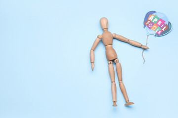 Wooden mannequin and paper air balloon with text APRIL FOOL'S on color background