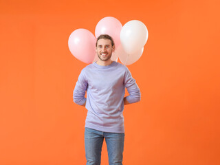 Handsome young man with balloons on color background