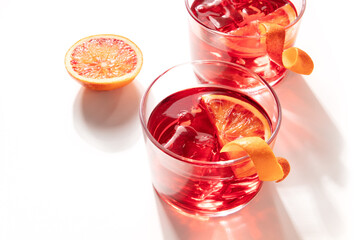 Negroni cocktails with blood oranges and ice on a white background, with shadows