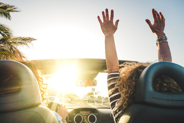 Happy lifestyle women couple enjoy travel with convertible car dancing and driving in the sunset - concept of joyful leisure transport trip activity for friends people having fun together - summer  - obrazy, fototapety, plakaty
