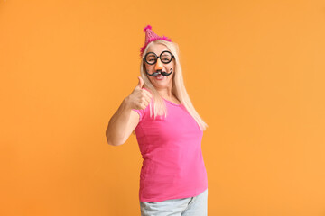 Mature woman in funny disguise showing thumb-up on color background. April Fools Day celebration