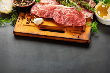Fototapeta na wymiar Fresh beef meat on cutting board on dark background with ingredients for cookin