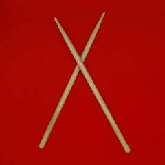 Detail of crossed percussion drumsticks on a red background.
