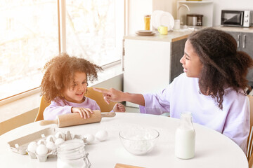 Cute African-American sisters cooking in kitchen