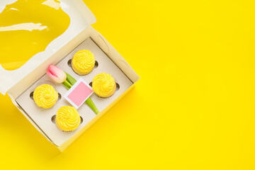 Box with tasty cupcakes and tulip flower on color background