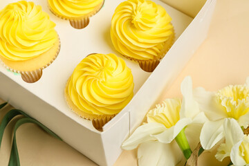 Box with tasty cupcakes and narcissus flowers on color background