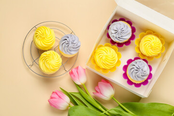 Box with tasty cupcakes and tulip flowers on color background