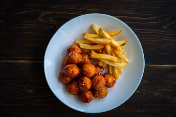 Spicy coated meatballs with spicy sauce served with fried potatoe fries. Korean style snacking.