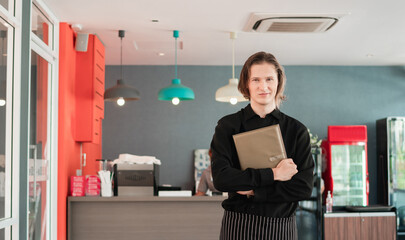 Coffee shop worker standing with holding menus serving in bar restaurant. Young man waitress carrying a menu at the counter