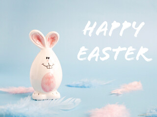 Cute white ceramic easter bunny or rabbit on blue background with feathers . Minimal Holiday concept. Symbol Happy Easter holiday. Creative. Copy space