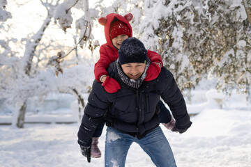 Fototapeta na wymiar Young Caucasian dad is rolling his 6 year old daughter on his back in a winter park. Snow and family games in winter.
