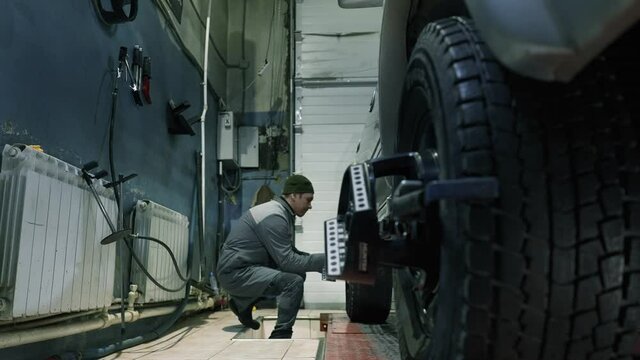 The car mechanic puts special sensors on the wheels to adjust the wheel camber.