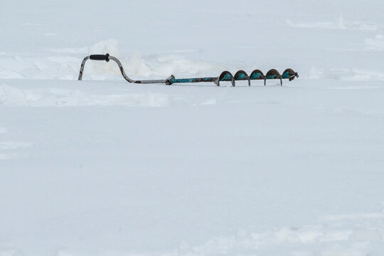 The drill for drilling holes in the ice lies on the snow. Advertising products for winter fishing with a place for text.