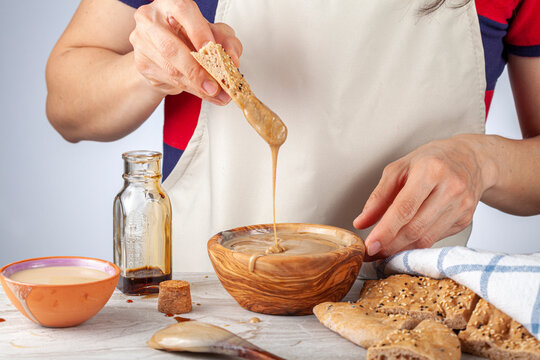 A caucasian woman wearing apron is dipping turkish pide (flat bread) with sesame and poppy seeds into traditional Turkish tahin pekmez desert made by mixing tahini with grape molasses. Delicious...