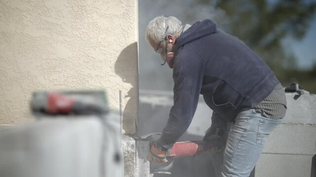 White caucasian elder worker doing concrete cutting work with angle grinder