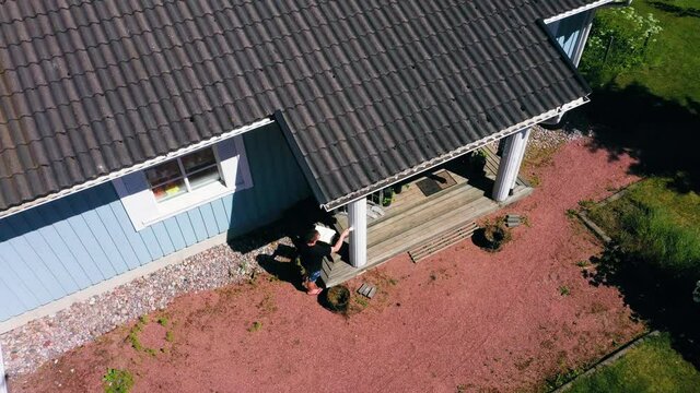 Aerial view of a man, painting a house white - descending, tilt up, drone shot