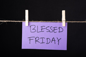  Blessed Friday word written on a Purple color sticky note hanging with a wire on black background.