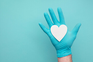 Doctors hands wearing blue surgical gloves holding a white heart shape