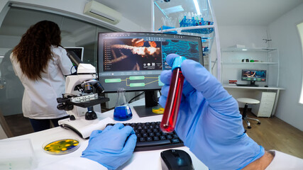POV of virologist doctor holding tube with blood sampe typing information in pc, analysing patient disease, examining virus evolution. Team of scientists doing research working in equipped laboratory.