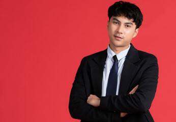 Portrait of young smart and handsome Asian male in blck suit posing with friendly face and self-confidence gesture on red background