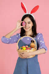 Young Asian woman wearing a Bunny hairband, holding an Easter egg, covering her eyes and hold a basket full of colorful eggs with a smiling face. The concept of easter eggs festival 