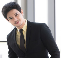 Asian man wearing a black suit is pictured with a straight face, slightly bowed and smiling at the corner of his mouth. In the concept of business people and work
