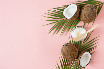 Obraz na płótnie Canvas Jar of coconut oil and fresh coconuts with palm leaves on pink background top view.