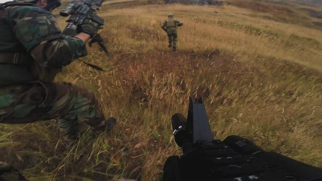 Point-of-view shot of squad of soldiers in camouflage uniform running through field armed with sniper rifles and guns