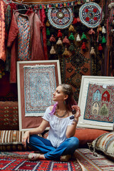 Obraz na płótnie Canvas Woman chooses carpet at the market. Oriental bazaar of textiles. Factory for the production of carpets. Cheerful joyful emotions on the face woman