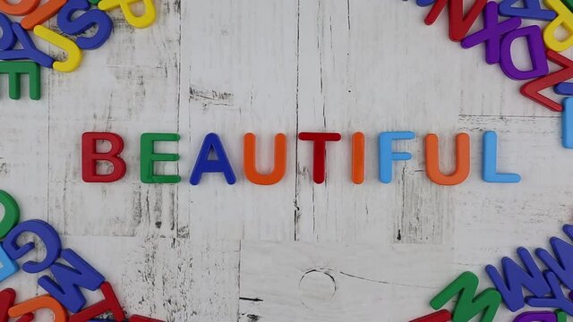 Colorful alphabet letters spelling the word - Beautiful - on a grey wooden background with corner decoration of further letters viewed from overhead. Stop motion, top view