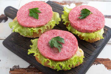 Sandwiches with lettuce leaves and sliced salami sausage on a wooden Board.