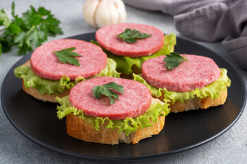 Sandwiches with lettuce leaves and sliced salami sausage on black plate.