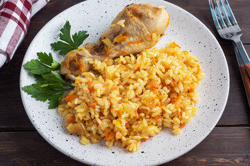 Delicious Asian pilaf, stewed rice with vegetables and chicken drumstick on a plate. Wooden rustic background.