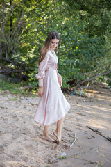 Fototapeta premium A beautiful woman in a light summer dress near the river.